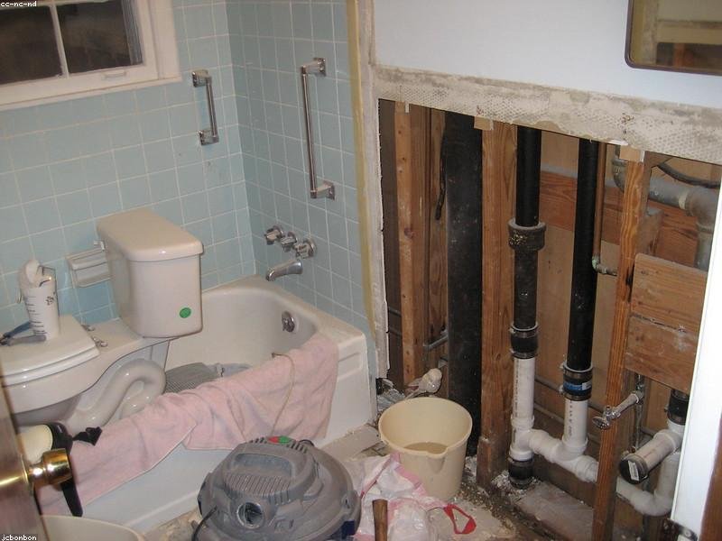 Bathroom mid-renovation with exposed plumbing and demolition debris